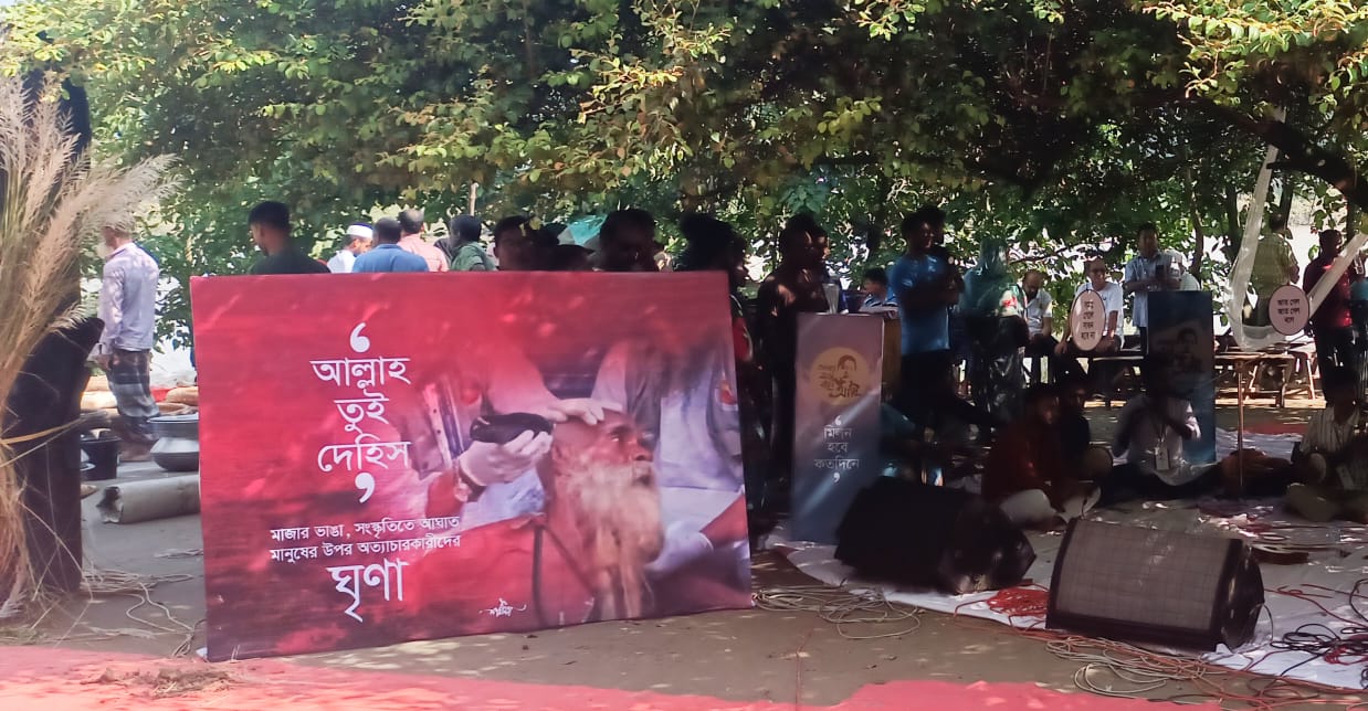 অনুষ্ঠানের একটি ব্যানারে লেখা ছিল, ‘আল্লাহ তুই দেহিস: মাজার ভাঙার সংস্কৃতিতে আঘাত, মানুষের ওপর অত্যাচারকারীদের ঘৃণা।’ ছবি: সংগৃহীত